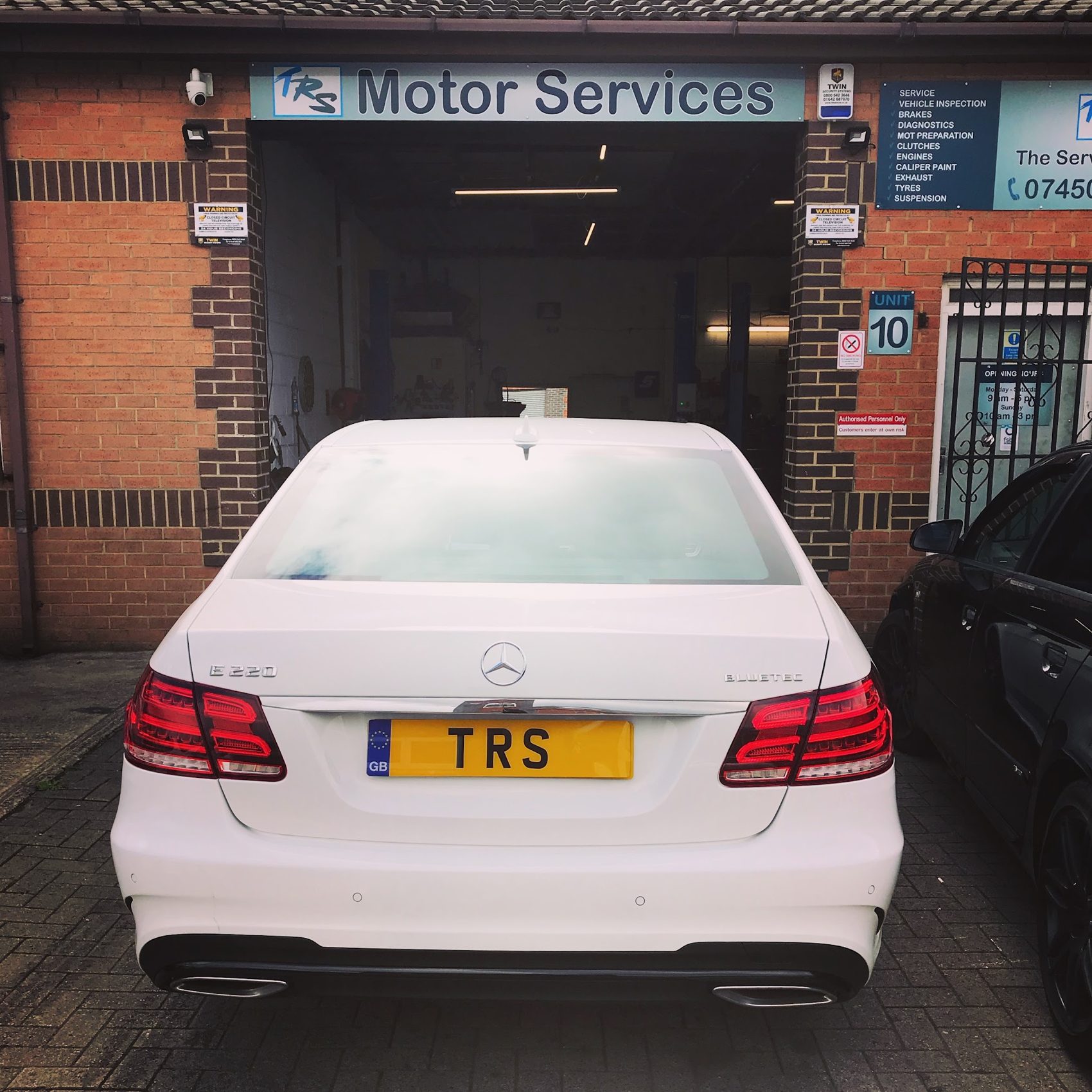 A white Mercedes with a TRS plate in front of the bay under the TRS Motor Services sign