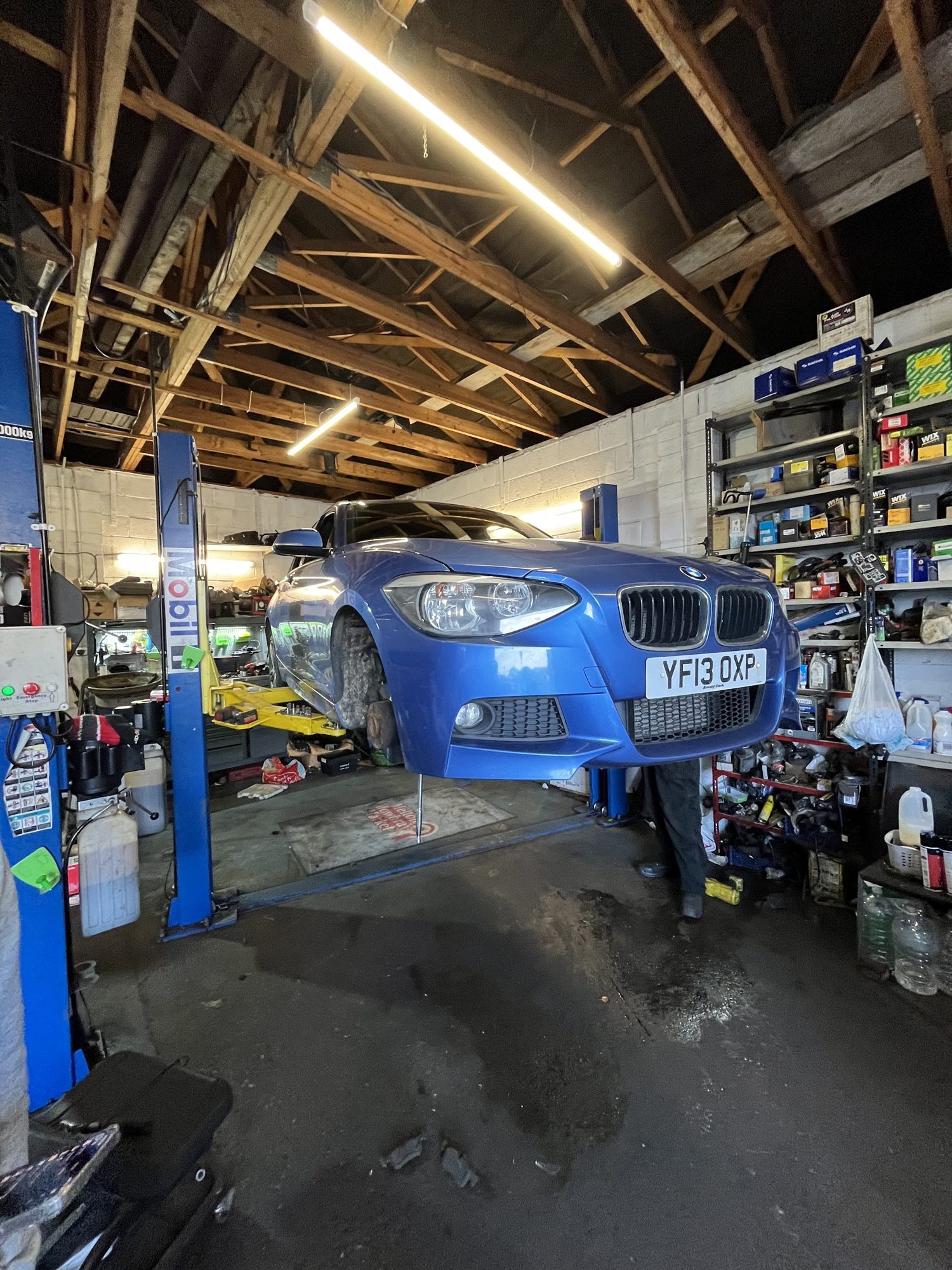 A blue BMW raised on a two-post lift in the workshop