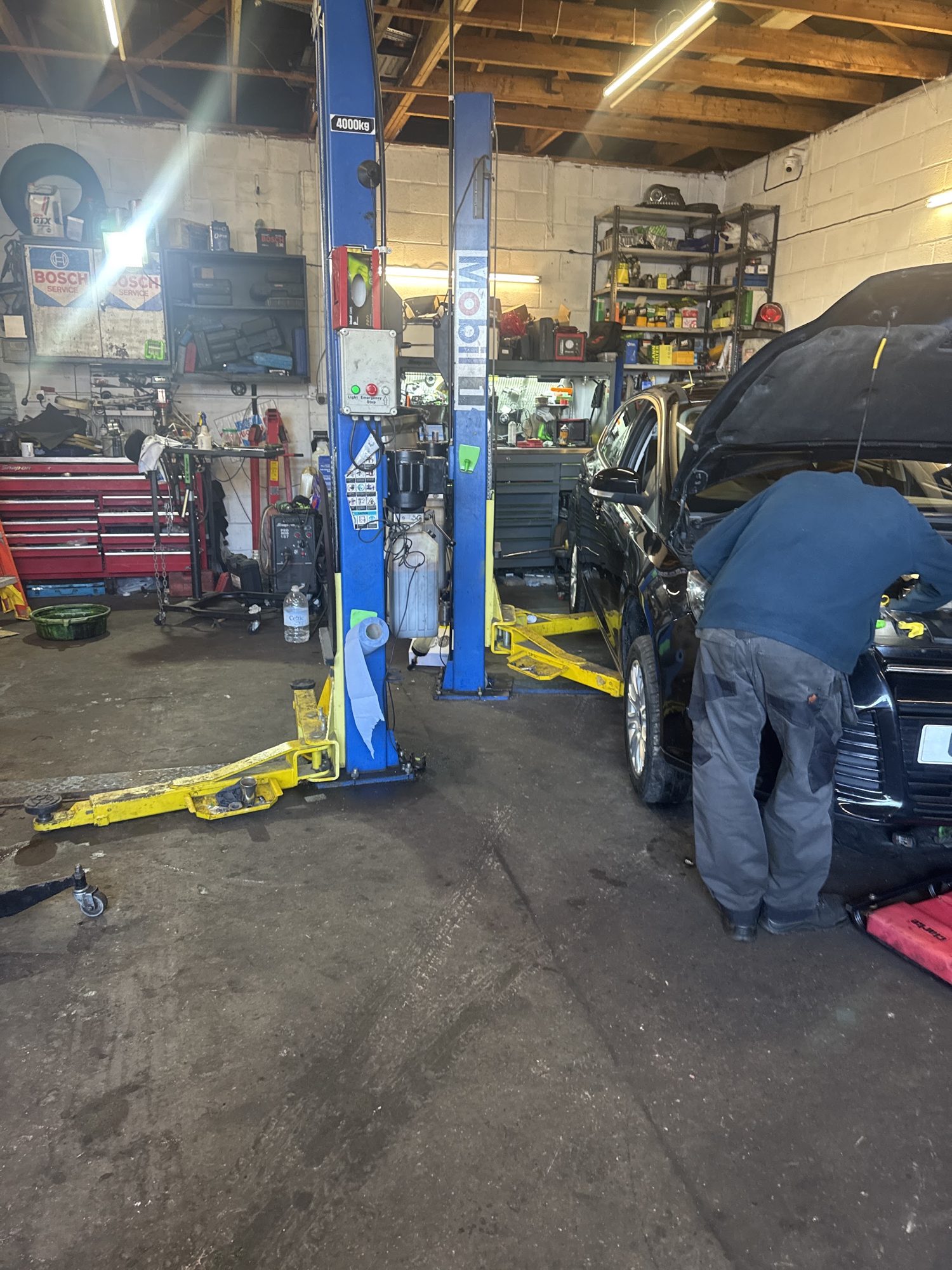 A mechanic working under the bonnet beside a lift