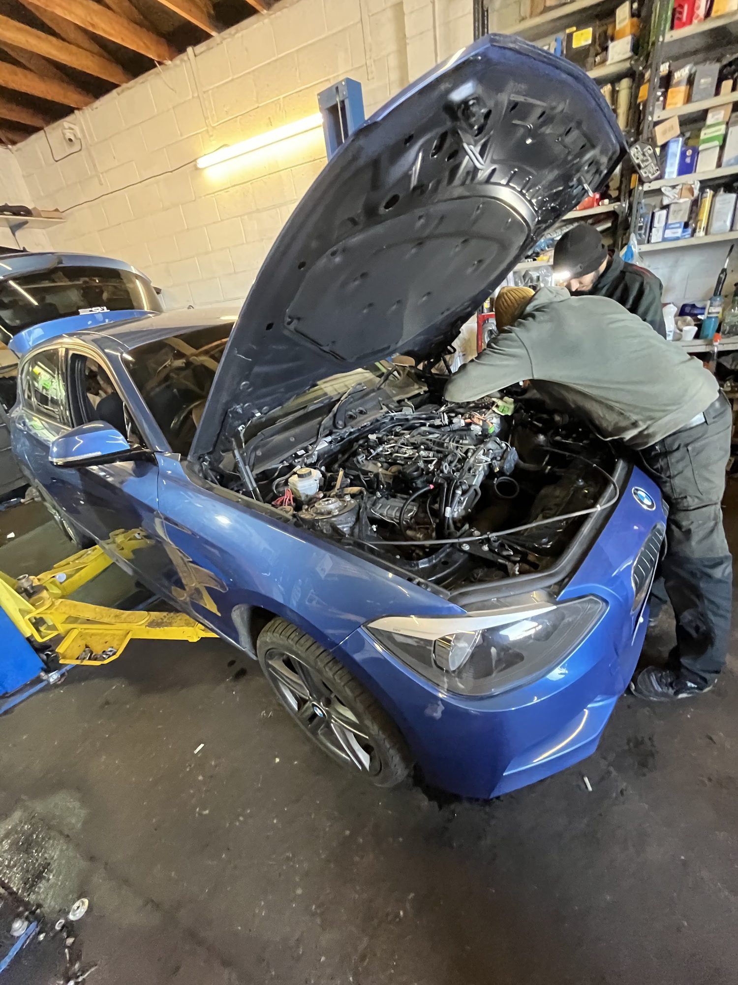 A blue BMW with its bonnet open and a mechanic at work on the engine